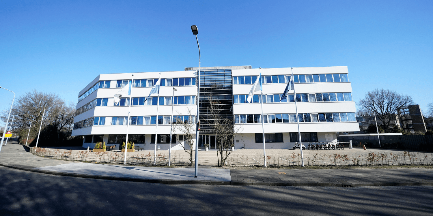 Front side of Amrâth Apart-Hotel Schiphol Badhoevedorp, modern white building with glass entrance and flagpole.